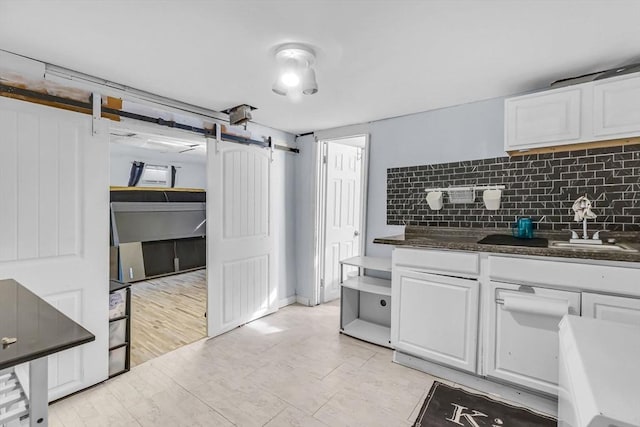 kitchen featuring white cabinetry, dark stone counters, a barn door, and decorative backsplash