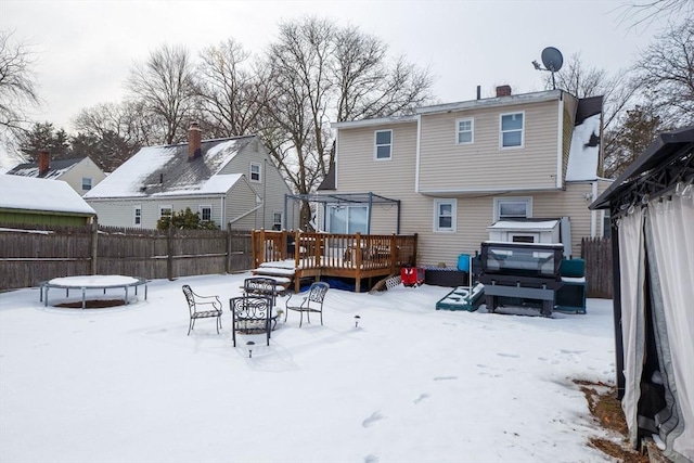 snow covered back of property with a trampoline, an outdoor fire pit, and a deck