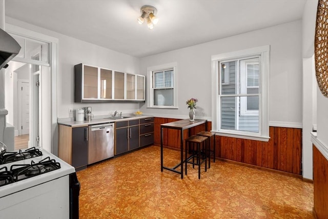 kitchen featuring light floors, white range with gas stovetop, wood walls, wainscoting, and dishwasher