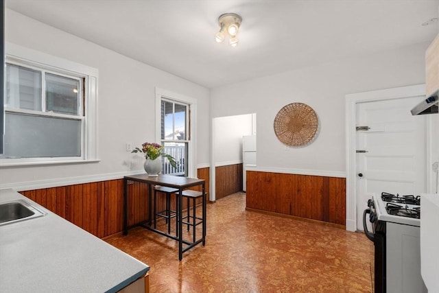 kitchen with brown cabinetry, light floors, freestanding refrigerator, gas range oven, and wainscoting