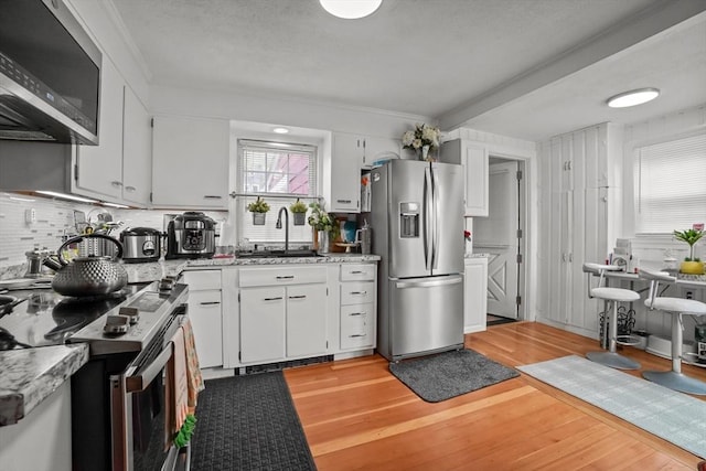 kitchen featuring decorative backsplash, appliances with stainless steel finishes, light wood-type flooring, a sink, and white cabinets