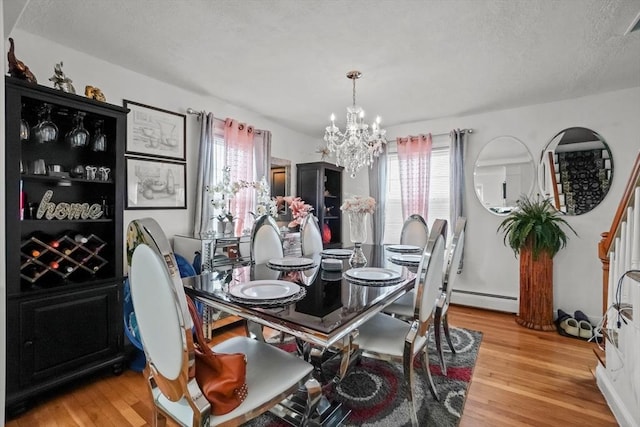 dining area featuring a textured ceiling, an inviting chandelier, baseboard heating, and light wood finished floors