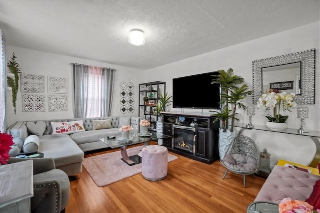 living area with a textured ceiling, a glass covered fireplace, and light wood-style floors