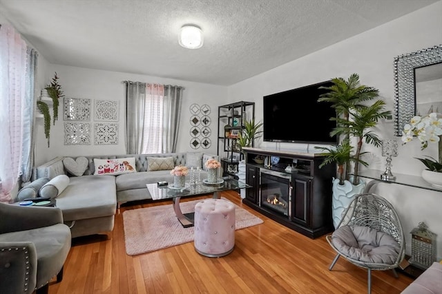 living area with a glass covered fireplace, a textured ceiling, and wood finished floors