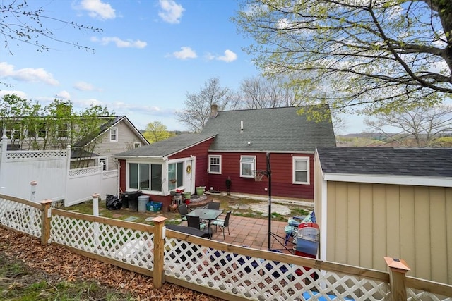 rear view of house featuring roof with shingles, fence, and a patio