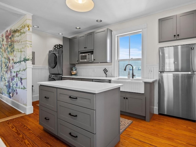5 Tremont St Unit 3, Cambridge, MA 02139 - kitchen featuring appliances with stainless steel finishes, gray cabinetry, stacked washer / drying machine, a sink, and wainscoting
