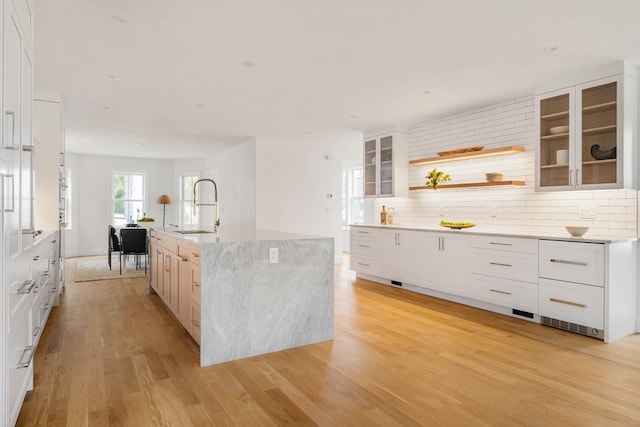 kitchen featuring white cabinets, sink, tasteful backsplash, a center island with sink, and light hardwood / wood-style floors