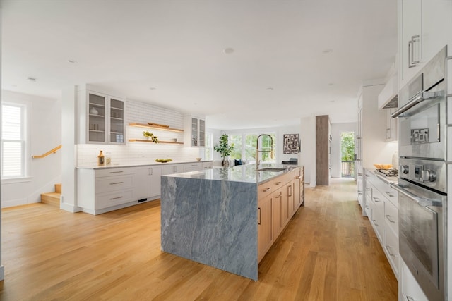 kitchen featuring light hardwood / wood-style floors, white cabinets, backsplash, a center island with sink, and sink