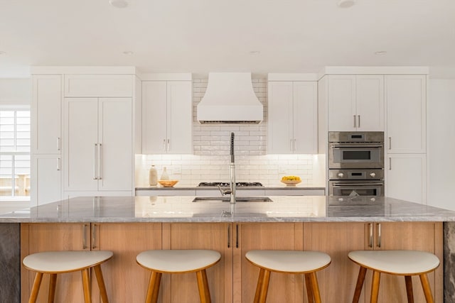 kitchen featuring light stone countertops, white cabinets, a spacious island, and custom exhaust hood