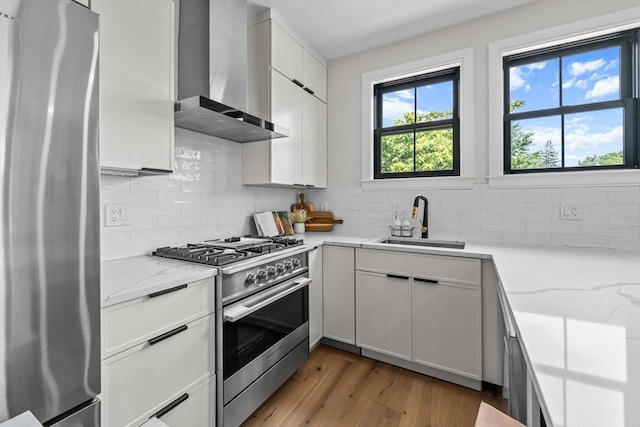 kitchen with white cabinets, wall chimney range hood, sink, light hardwood / wood-style flooring, and stainless steel appliances