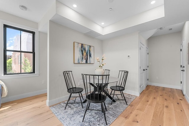 dining space featuring a raised ceiling and light wood-type flooring