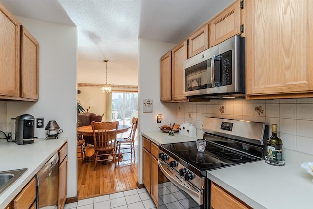 kitchen with light brown cabinetry, hanging light fixtures, light tile patterned floors, stainless steel appliances, and decorative backsplash