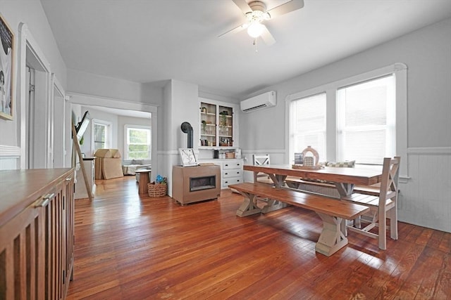 180 Irvington St, New Bedford, MA 02745 - dining room featuring a wall unit AC, ceiling fan, a wainscoted wall, hardwood / wood-style flooring, and a fireplace
