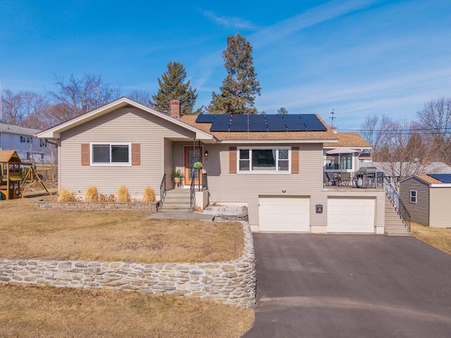 single story home featuring a chimney, a front lawn, a garage, aphalt driveway, and roof mounted solar panels