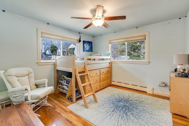 bedroom with light wood finished floors, multiple windows, and a baseboard heating unit