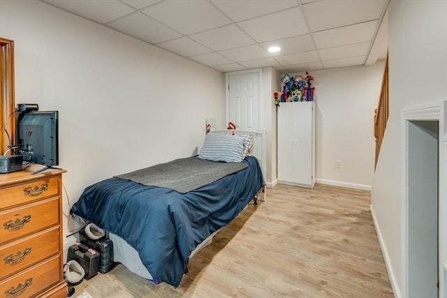 bedroom featuring a paneled ceiling, baseboards, and light wood finished floors