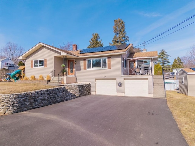 ranch-style house with a front yard, solar panels, a chimney, a garage, and aphalt driveway