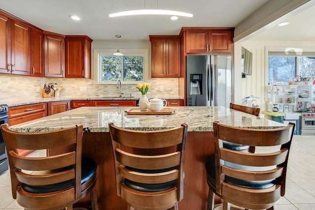 kitchen with light stone counters, stainless steel fridge with ice dispenser, a sink, backsplash, and a center island