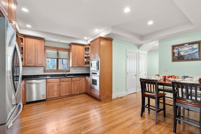 kitchen featuring brown cabinets, dark countertops, a sink, light wood-style floors, and stainless steel appliances