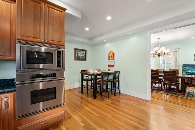 kitchen with a notable chandelier, baseboards, appliances with stainless steel finishes, and light wood finished floors