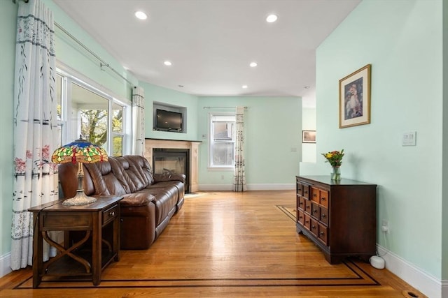 living area featuring baseboards, a glass covered fireplace, plenty of natural light, and light wood-style floors