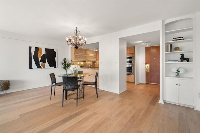 dining space featuring built in shelves, an inviting chandelier, and light hardwood / wood-style flooring