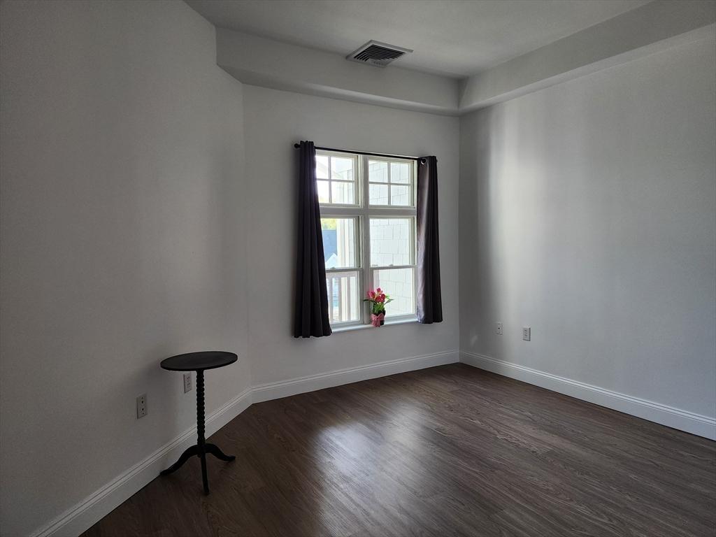 unfurnished room featuring baseboards, dark wood-style floors, and visible vents