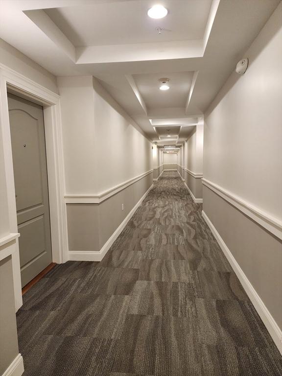 corridor with baseboards, carpet, and a raised ceiling