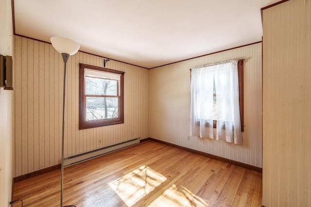 spare room featuring a baseboard heating unit, light wood finished floors, ornamental molding, and baseboards