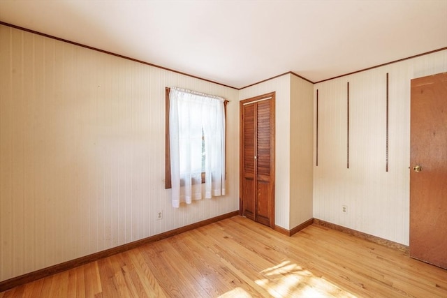 unfurnished bedroom featuring light wood-style floors, a closet, crown molding, and baseboards