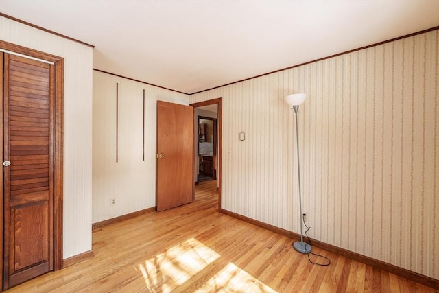 empty room featuring ornamental molding, light wood-type flooring, and baseboards