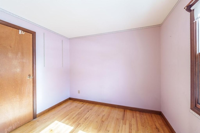 empty room with crown molding, baseboards, and light wood-style floors