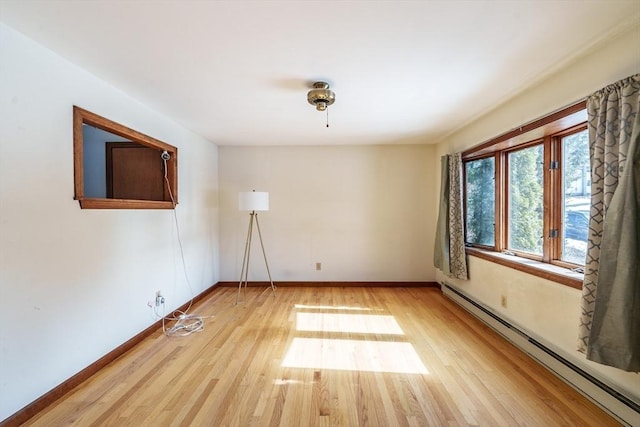 spare room with a baseboard heating unit, light wood-type flooring, and baseboards