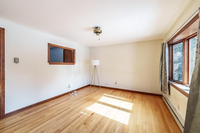 spare room with baseboards, a baseboard heating unit, and wood finished floors