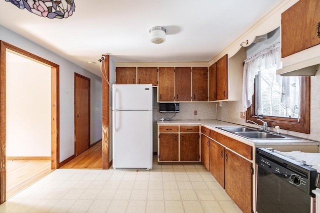 kitchen featuring a sink, black dishwasher, light countertops, freestanding refrigerator, and light floors