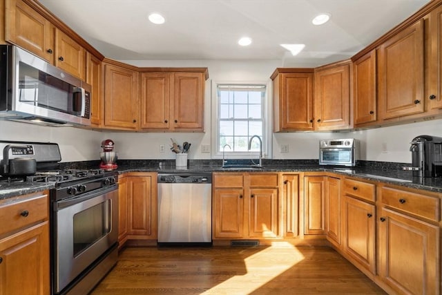 kitchen featuring dark wood-type flooring, recessed lighting, appliances with stainless steel finishes, brown cabinetry, and a sink