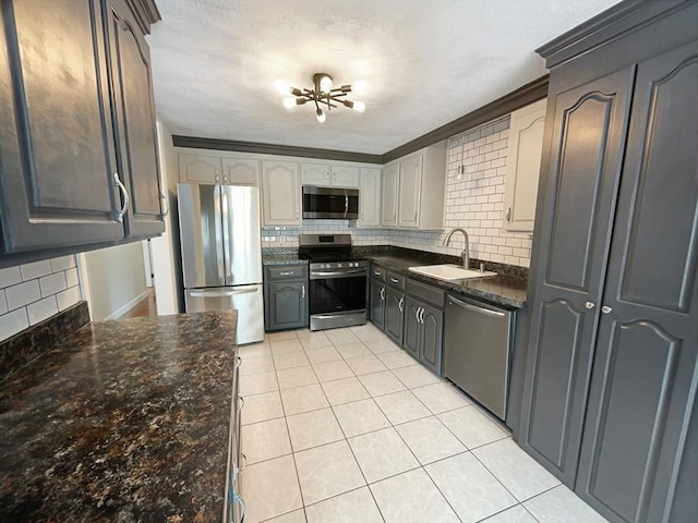 kitchen featuring light tile patterned floors, dark stone counters, a sink, stainless steel appliances, and backsplash