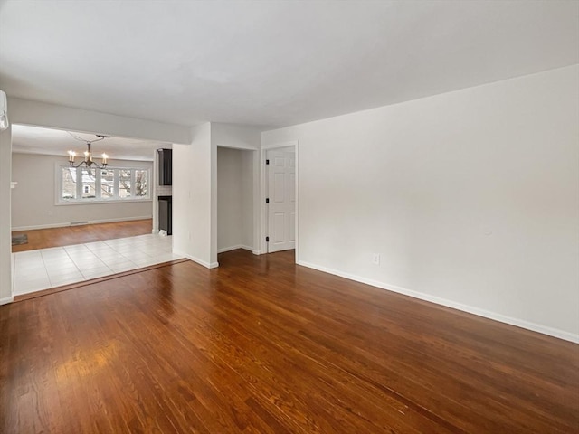 unfurnished living room with a notable chandelier, baseboards, and wood finished floors