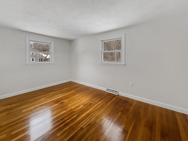 unfurnished room with wood-type flooring, visible vents, and baseboards