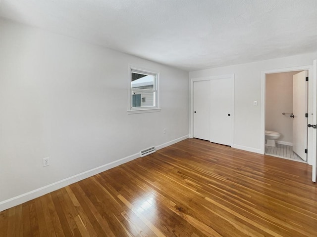 unfurnished bedroom featuring ensuite bathroom, wood finished floors, visible vents, and baseboards