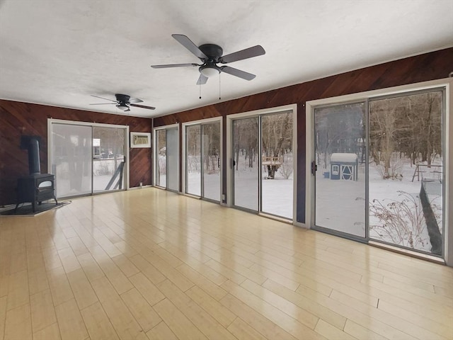 unfurnished sunroom featuring a wood stove, a healthy amount of sunlight, ceiling fan, and a wall mounted AC