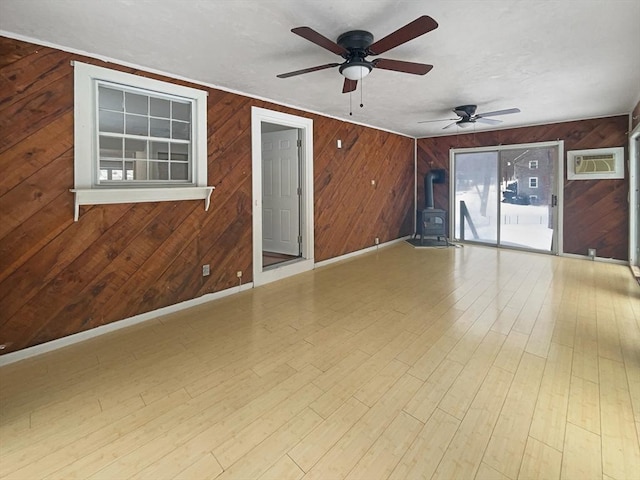 empty room featuring a wood stove, wood walls, baseboards, and wood finished floors