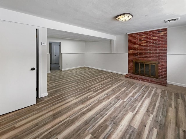 finished basement featuring a textured ceiling, a fireplace, wood finished floors, and visible vents