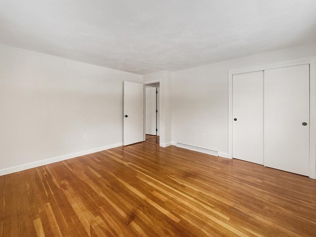 unfurnished bedroom featuring a closet, baseboards, baseboard heating, and wood finished floors