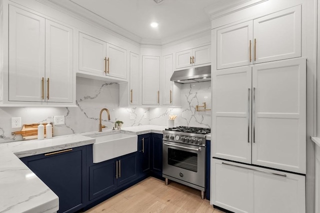 kitchen featuring premium appliances, white cabinetry, a sink, blue cabinets, and under cabinet range hood