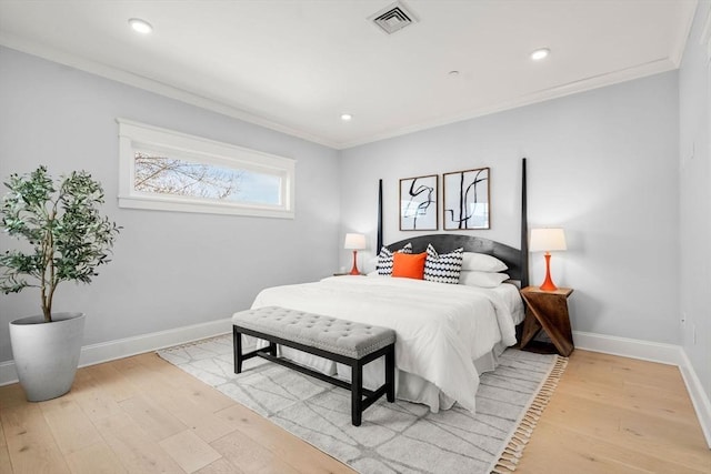 bedroom with light wood finished floors, visible vents, baseboards, and crown molding