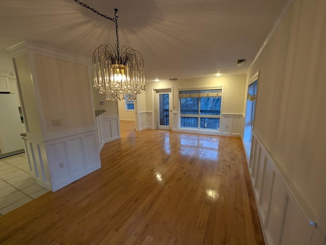 unfurnished dining area with ornamental molding, an inviting chandelier, and light wood-type flooring