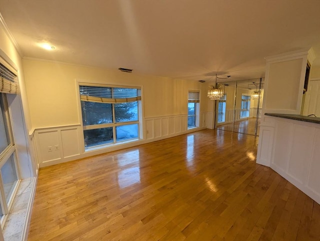 unfurnished living room featuring a notable chandelier, crown molding, and light wood-type flooring