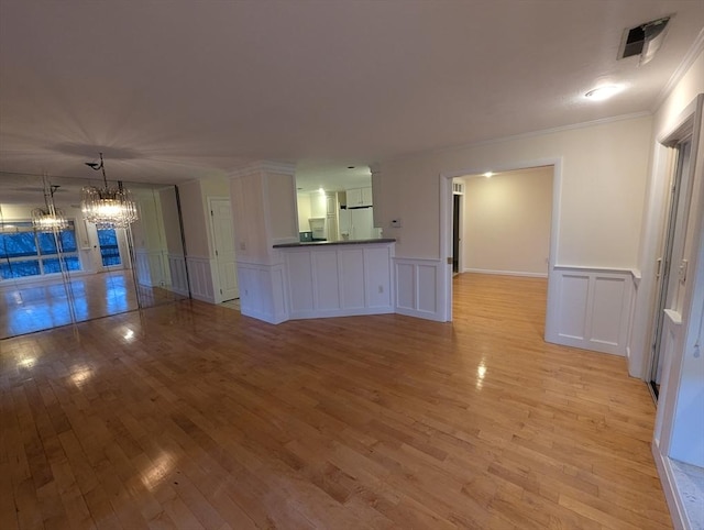 unfurnished living room featuring crown molding, a chandelier, and light hardwood / wood-style flooring