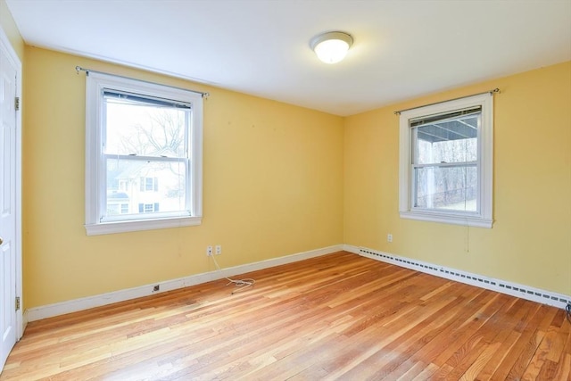 empty room with light wood-type flooring, a healthy amount of sunlight, and a baseboard heating unit